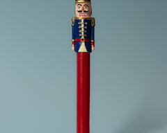 Sir Elliott nutcracker candle with a navy blue jacket and red stem in a black holder against a blue-grey background.