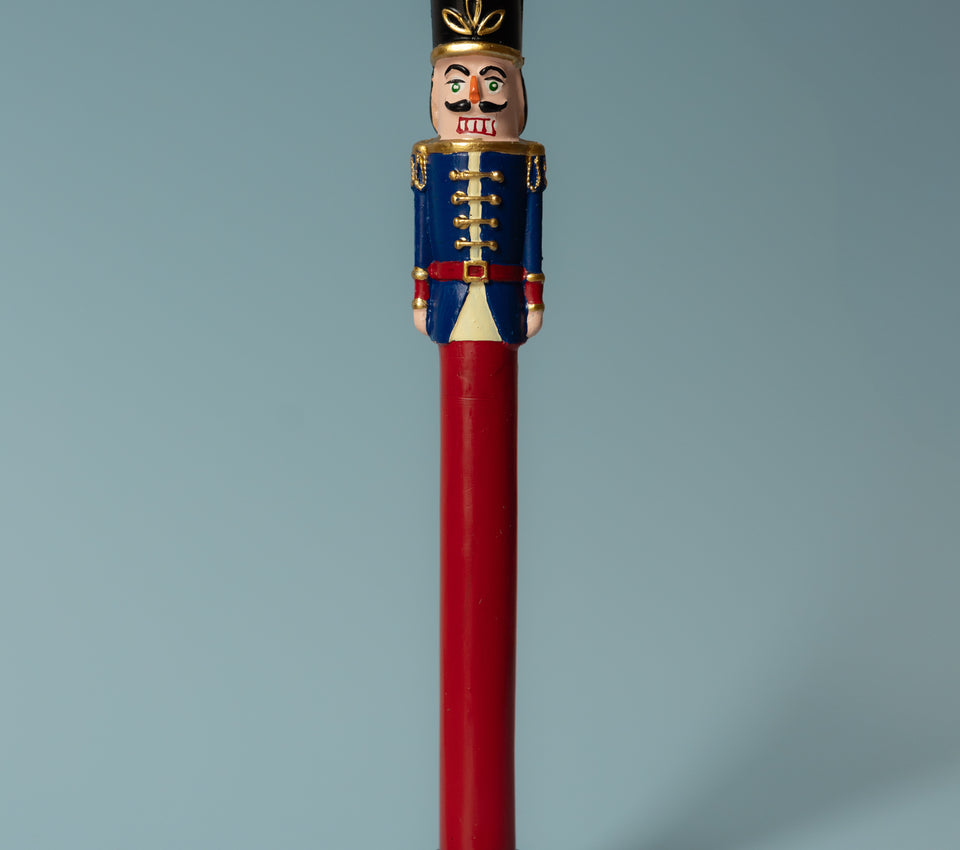 Sir Elliott nutcracker candle with a navy blue jacket and red stem in a black holder against a blue-grey background.